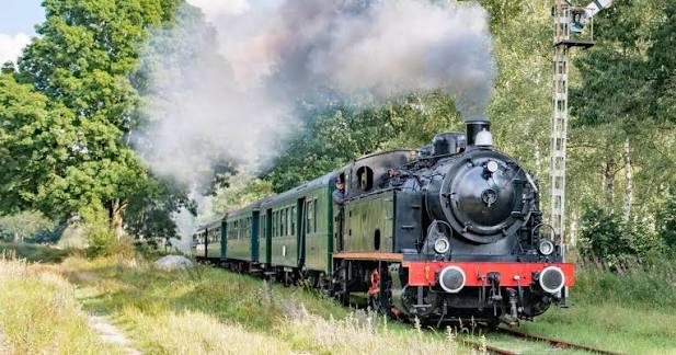 Classic European steam locomotive travelling through lush countryside